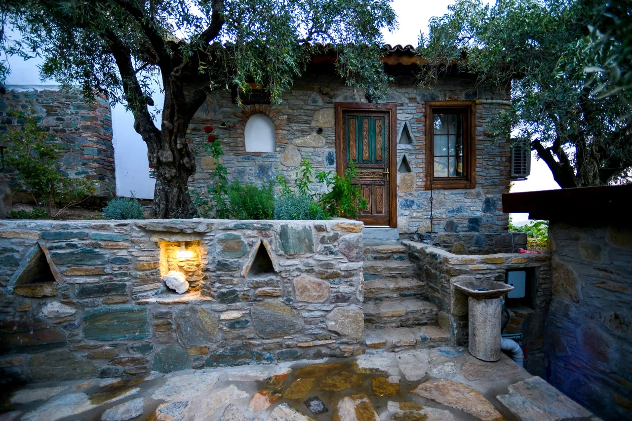 Taş House's stone exterior, wooden door and courtyard beneath olive branches