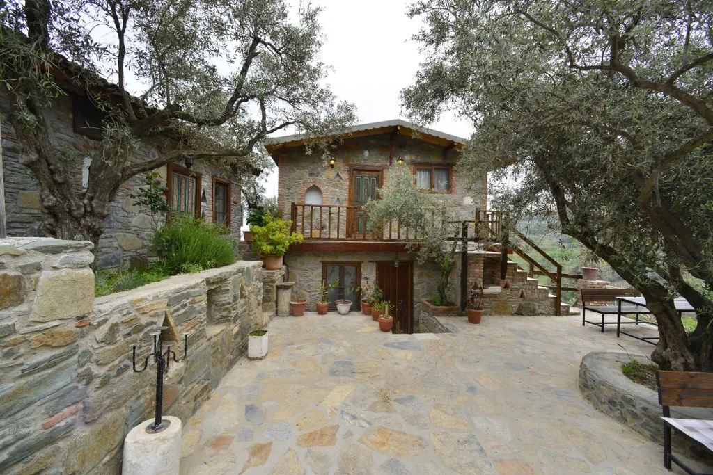 Zeytinli House's stone courtyard and exterior with wooden balcony among olive trees
