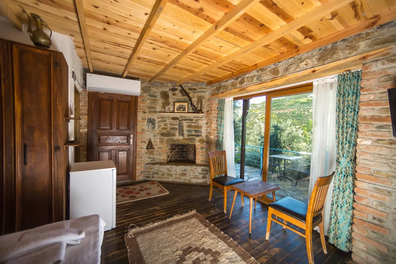 İncirli House's stone walls, wooden ceiling and seating area beside the glass doors